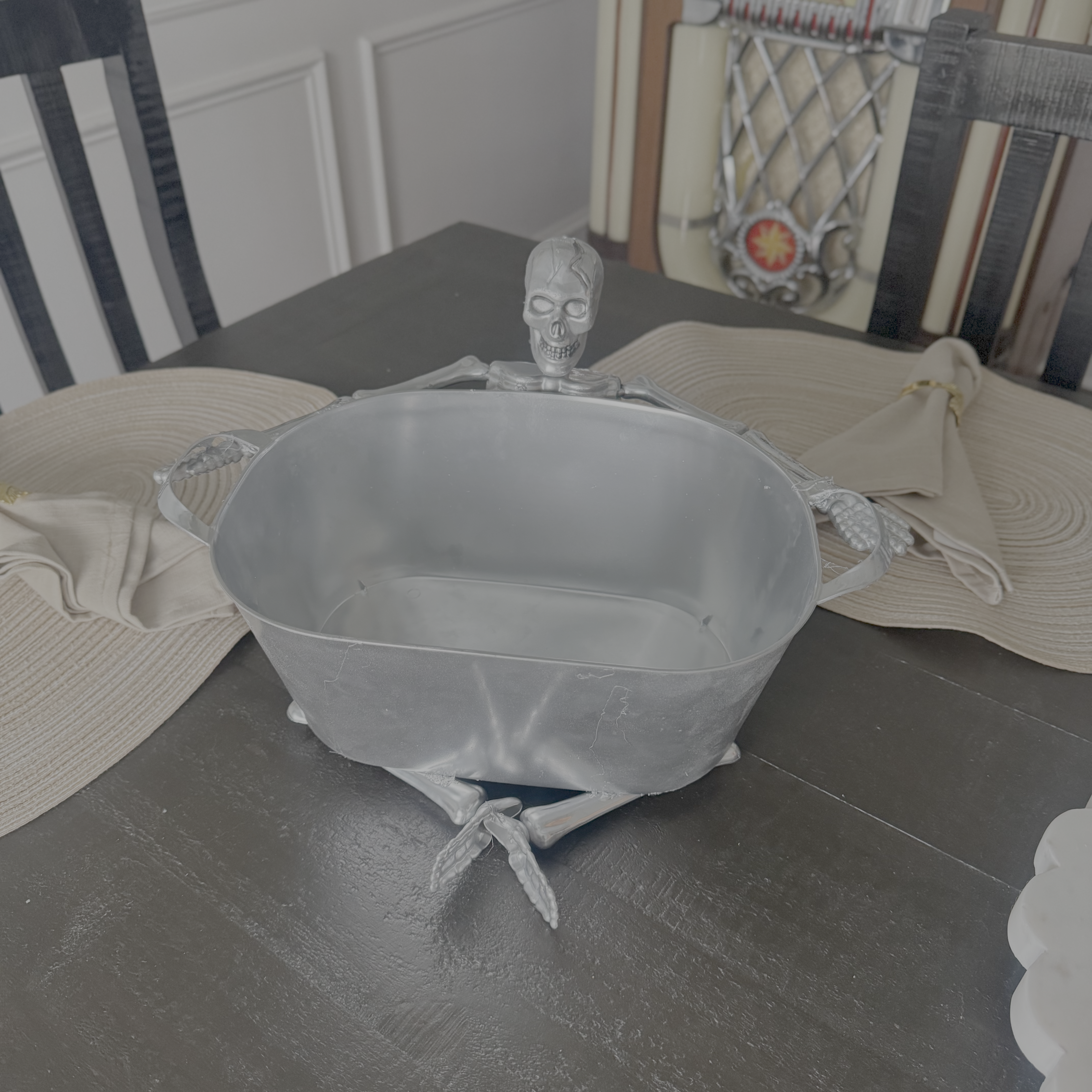 Finished DIY Halloween bowl made from a Dollar Tree plastic skeleton and silver spray-painted bowl, styled as a Pottery Barn-inspired candy dish centerpiece on a dining table.