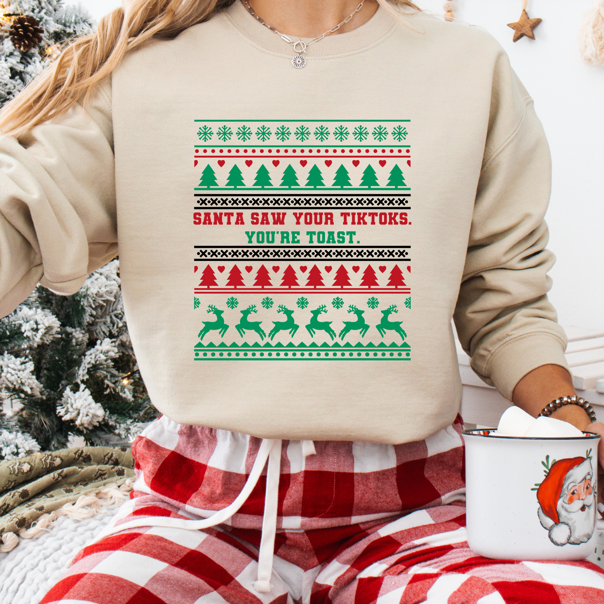 Beige sweatshirt with funny ugly sweater design that reads โSanta Saw Your TikToks. Youโre Toast.โ with trees, reindeer, and stripe patterns.