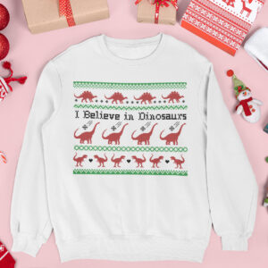 White Christmas sweatshirt with a red and green pixel-style design featuring dinosaurs and the phrase I Believe in Dinosaurs surrounded by holiday decor.