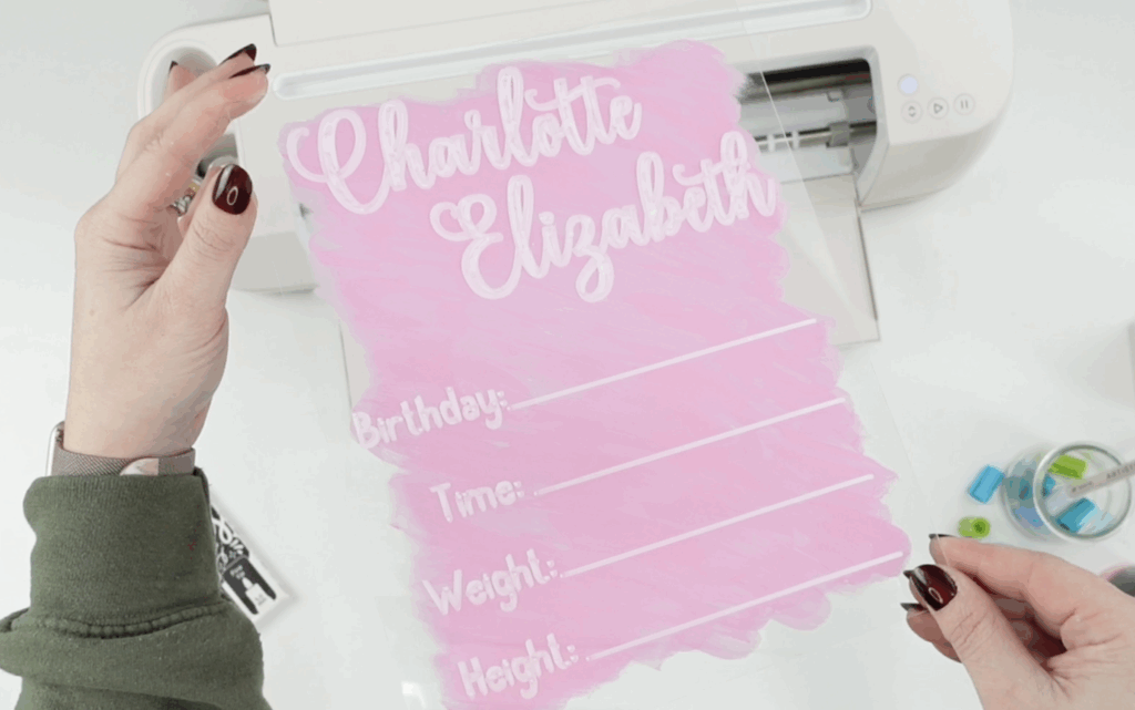 Finished acrylic baby announcement sign with white lettering and pink painted backing made using a Cricut and acrylic markers.