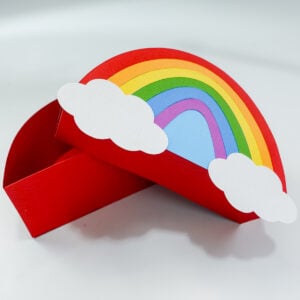 3D rainbow gift box made with a Cricut machine using a rainbow box SVG free file, showing the lid lifted and layered rainbow design with white clouds.