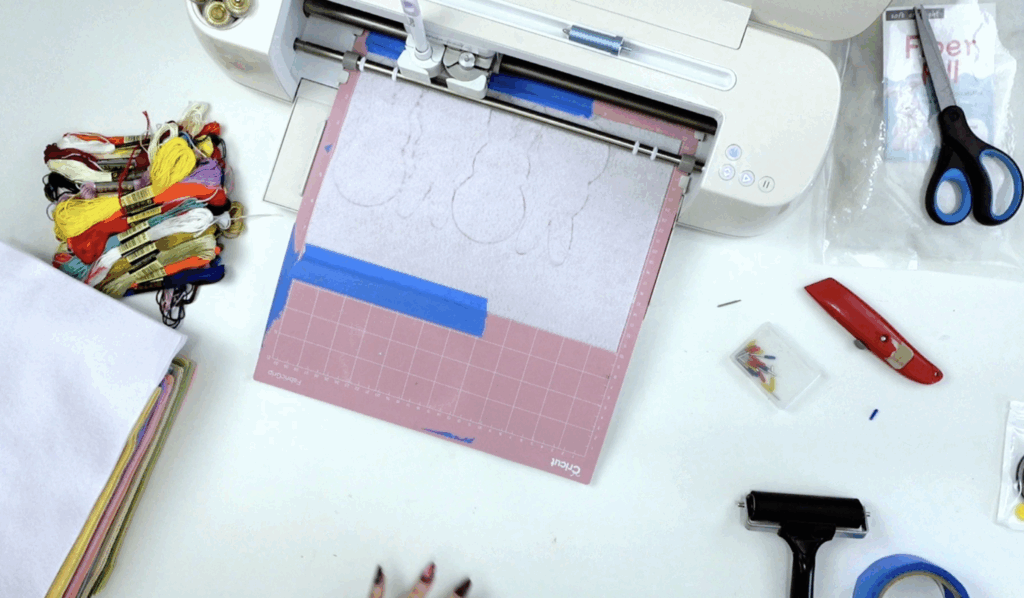White felt sheet placed on a pink Cricut cutting mat with painter’s tape before cutting shapes with a Cricut Maker.