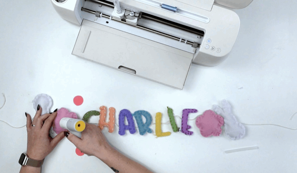 Hot glue attaching sewn felt banner pieces to twine string to assemble the finished name banner.