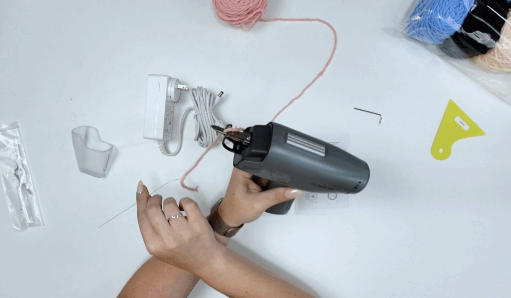 Hands threading pink yarn through the clawlab tufting gun using a wire threader tool.