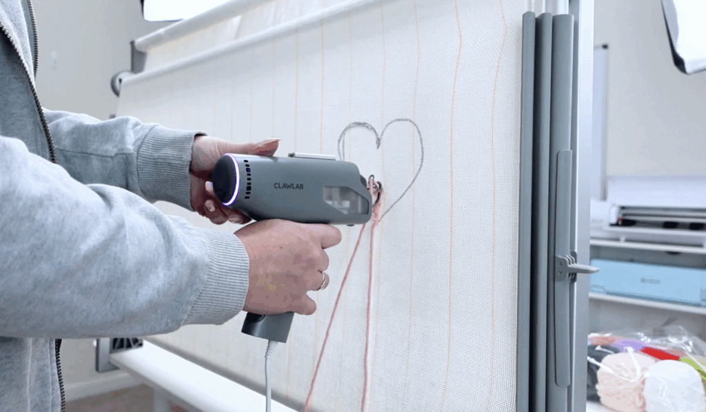 Clawlab tufting gun punching pink yarn into stretched tufting cloth while creating a heart design.