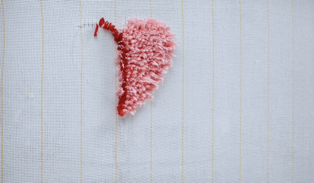 Small tufted heart made with pink yarn on primary tufting cloth during a beginner tufting test.