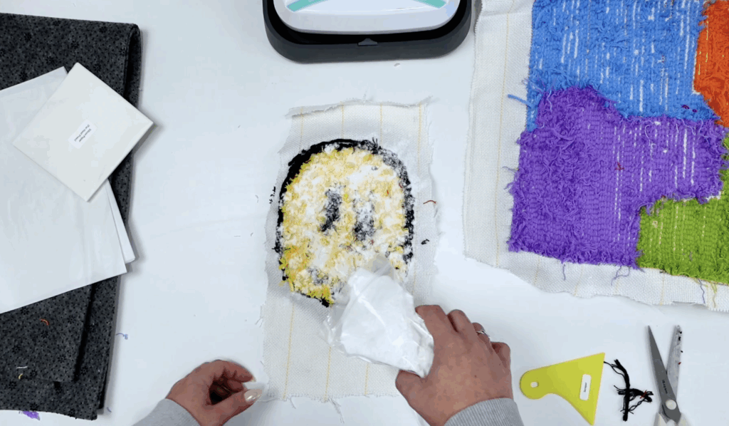 TPU hot melt glue powder being applied to the back of a tufted smiley face rug before attaching backing fabric.