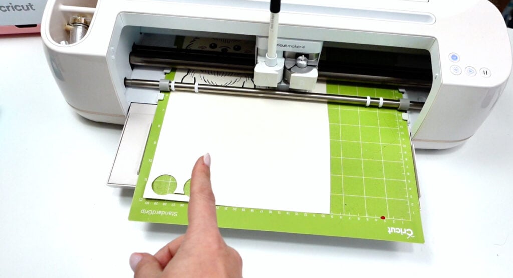 Cricut machine drawing AI-generated image with pen tool on cardstock mat.