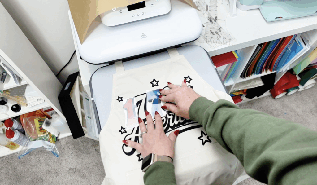 Applying the first HTV layer onto an apron using a heat press and knockout method.