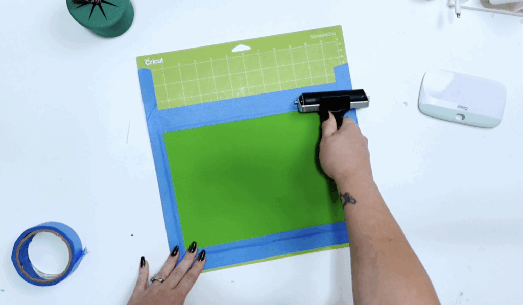 Green faux leather secured to a Cricut cutting mat with painter's tape and a brayer tool.